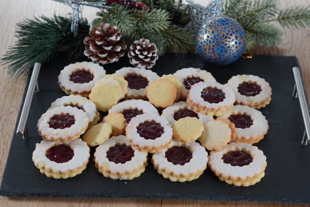 Linzer Augen und Spitzbuben auf einer schwarzen Schiefertafel – frisch gebacken und mit Puderzucker bestäubt
