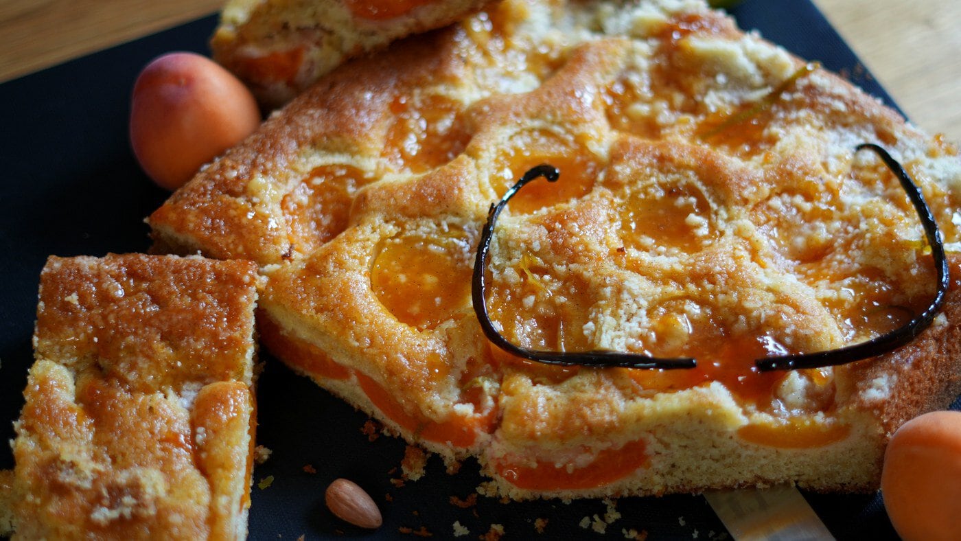 Fertiger Marillenkuchen auf dunkler Platte mit Stücken, Mandeln und Marillen als Dekoration.