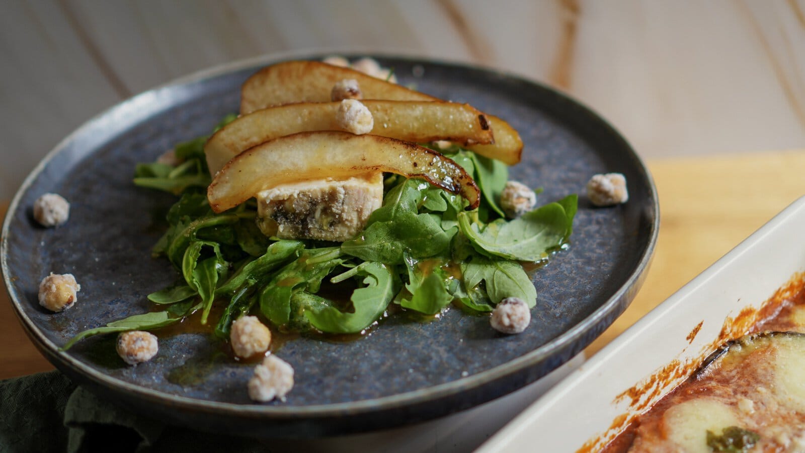 Rucola-Birnen-Salat mit Gorgonzola und kandierten Haselnüssen auf dunklem Teller