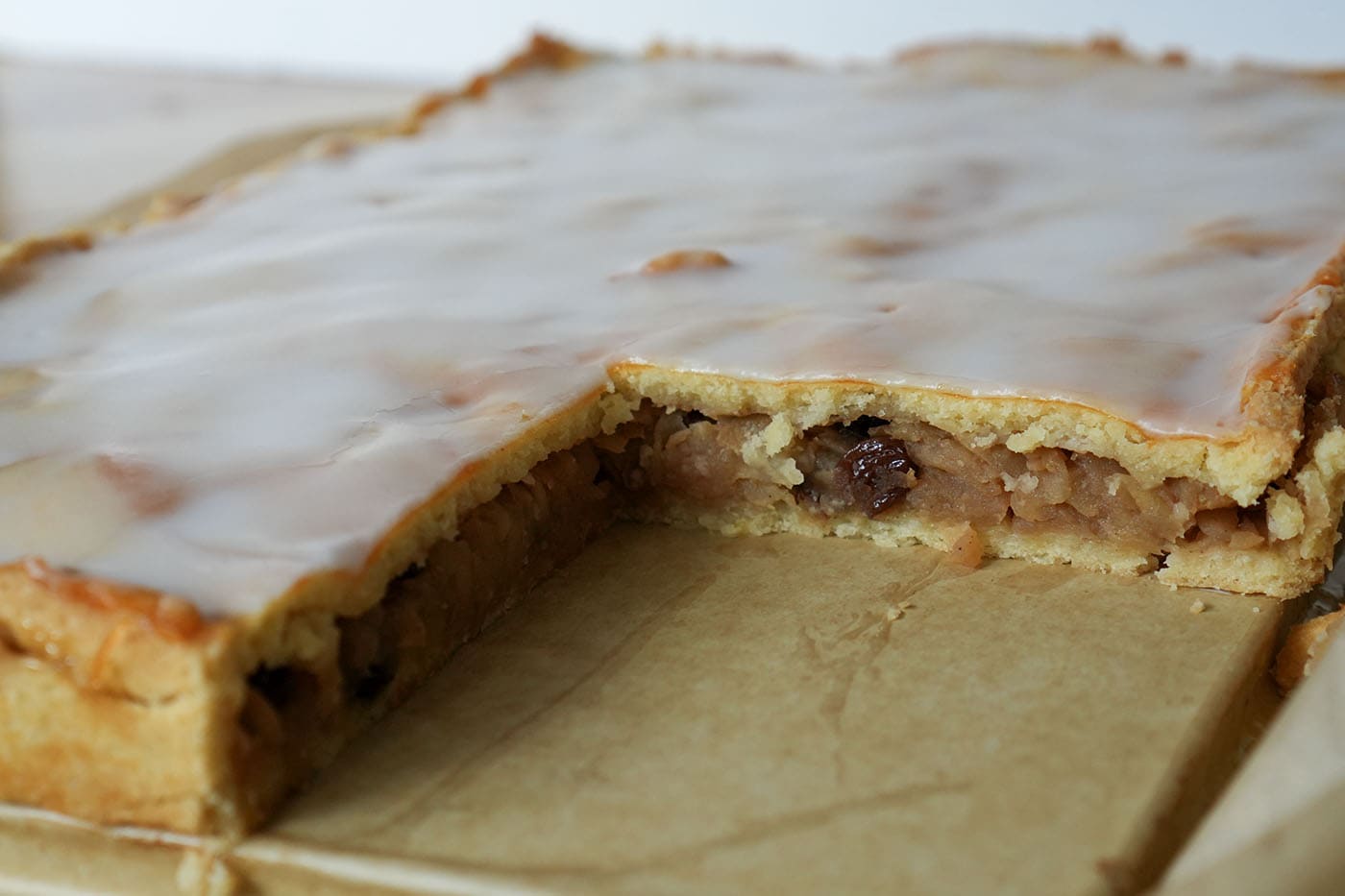 Angeschnittener gedeckter Apfelkuchen im Blech, die geraspelte Apfelfüllung steht als kompakte Schicht unter dem Mürbteig-Deckel