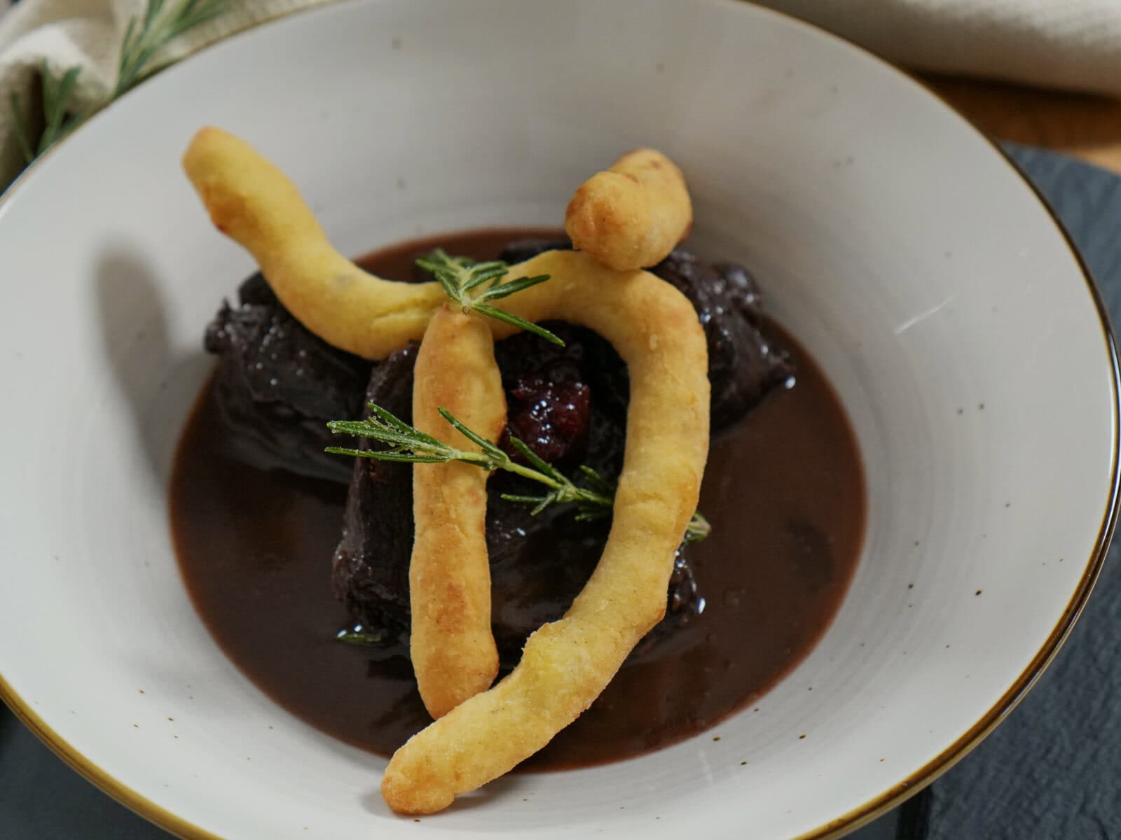 Hirschragout in dunkler Sauce von oben, darüber drei frittierte Erdäpfelnidei und Rosmarin.