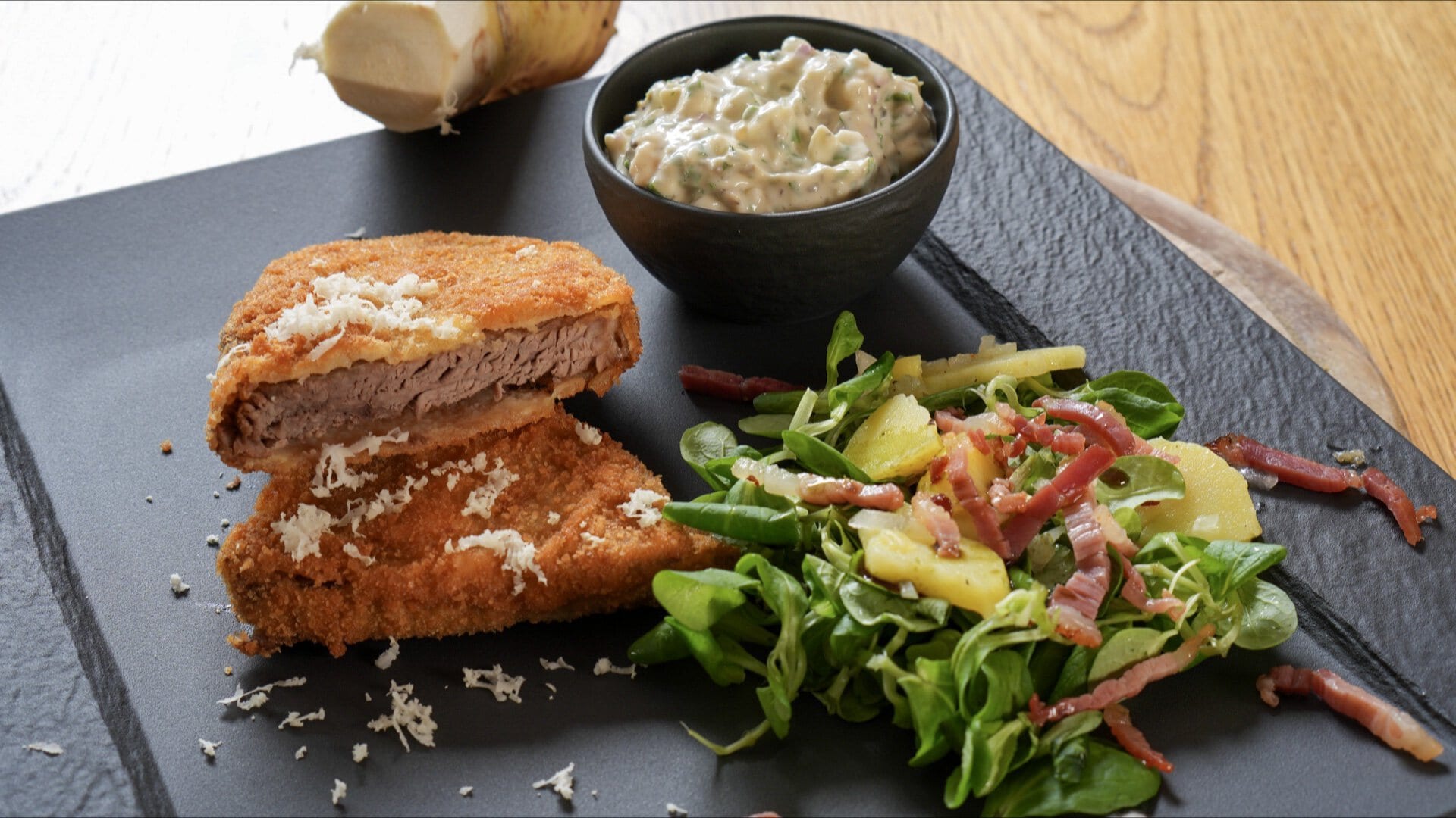 Alt-Wiener Backfleisch: zwei panierte Scheiben gekochter Tafelspitz mit geriebenem Kren auf Schieferplatte, daneben Erdäpfel-Vogerlsalat mit Speck und Sauce Tartare